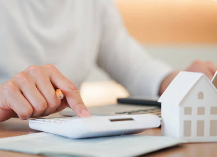 Themenbild Hausverwaltung Zu sehen ist eine Person am Schreibtisch mit einem Laptop, einem Taschenrechner und einem Dekohaus.